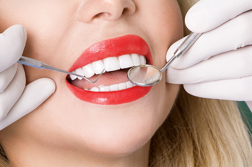 Dentist holding tools close to smiling womans mouth with white teeth on show